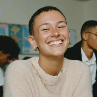 Happy teenager in a classroom. She has short cropped hair and wears a beige cashmere jumper.